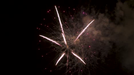 several fireworks explode in the night sky, leaving a trail of smoke