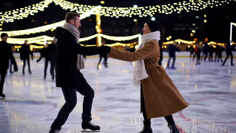 couple ice skating at night on an outdoor rink with festive lights