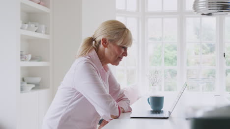 Reife-Frau-Zu-Hause,-Die-Einen-Videoanruf-Auf-Dem-Laptop-Auf-Der-Küchentheke-Führt