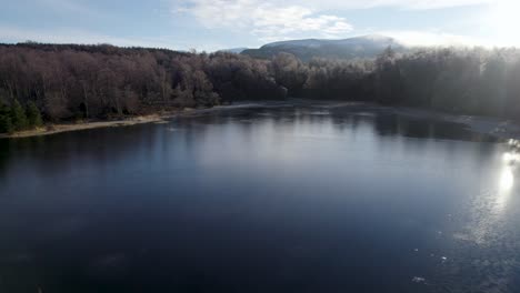 aerial drone footage reversing to reveal frost covered trees in a native forest and a frozen loch in a winter landscape on rothiemurchus estate in cairngorms national park, scotland