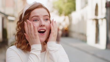 redhead woman looking surprised at camera shocked by sudden win good victory news wow in city street