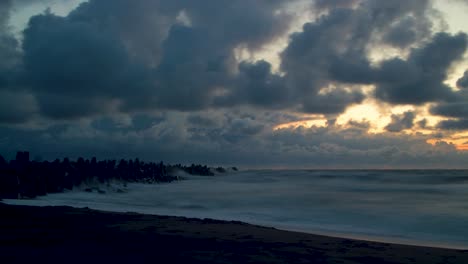 time lapse of fast moving dark dramatic storm clouds and big waves at the beach near the northern pier in liepaja at sunset, wide shot