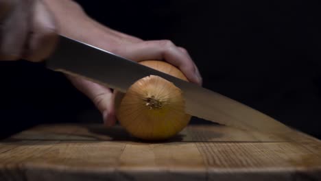 close up shot of lady cutting onions on cutting board with black background