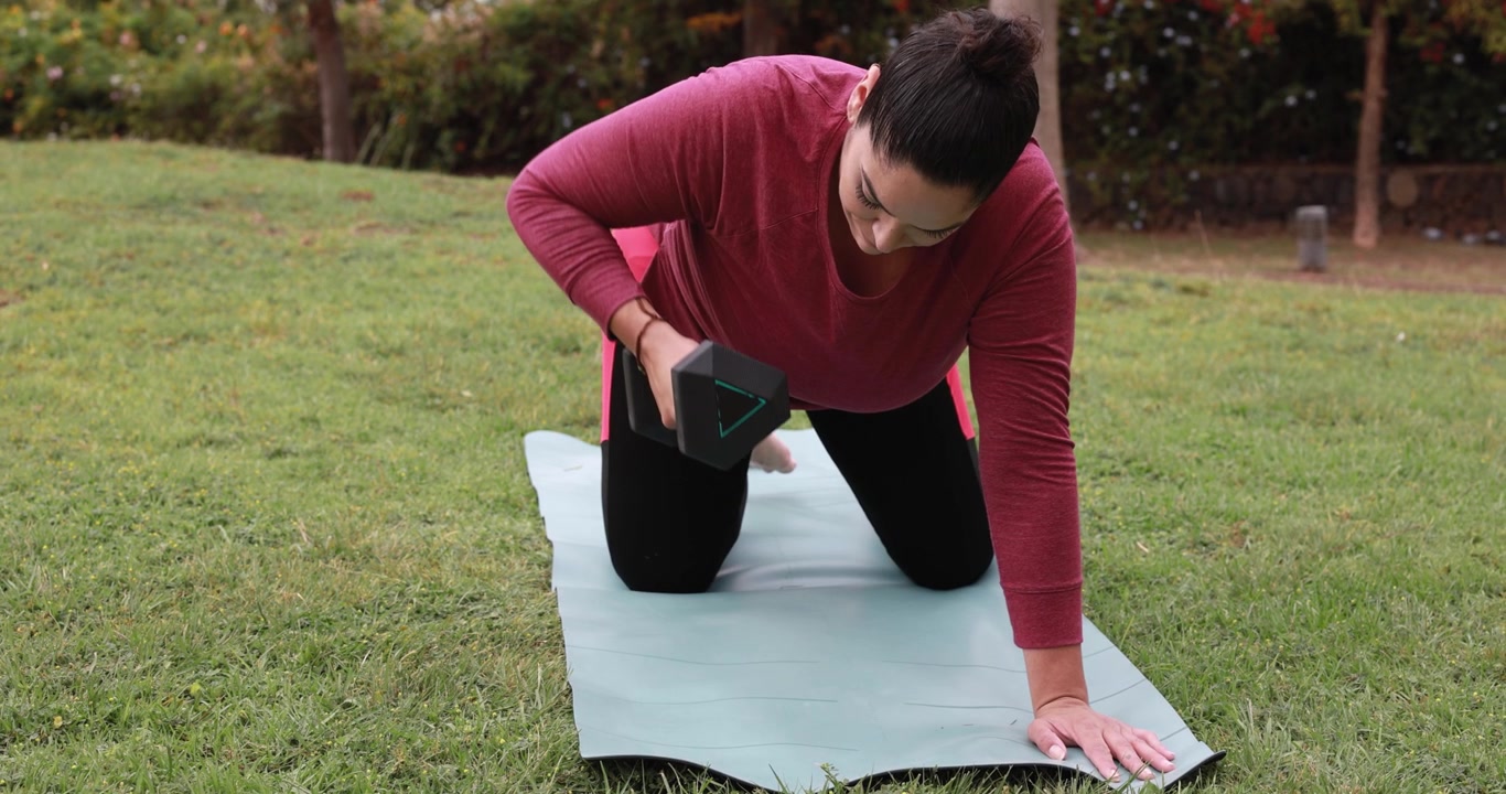 Mujer realizando remo con mancuernas en una esterilla de yoga en un parque