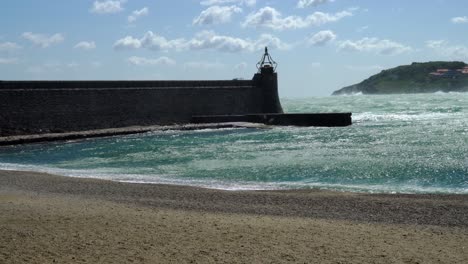 strong waves break around the harbour wall of collioure while heavy winds whip up the water which sprays on the wall