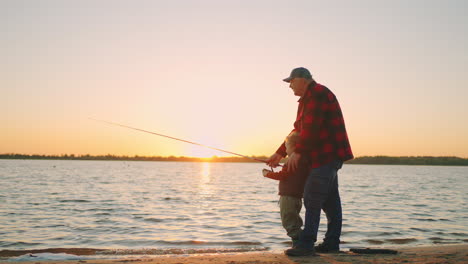 un viejo pescador está enseñando a su nieto a pescar el abuelo y el niño pequeño están de pie en la orilla