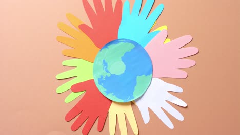 Close-up-of-hands-together-with-globe-made-of-colourful-paper-on-brown-background-with-copy-space