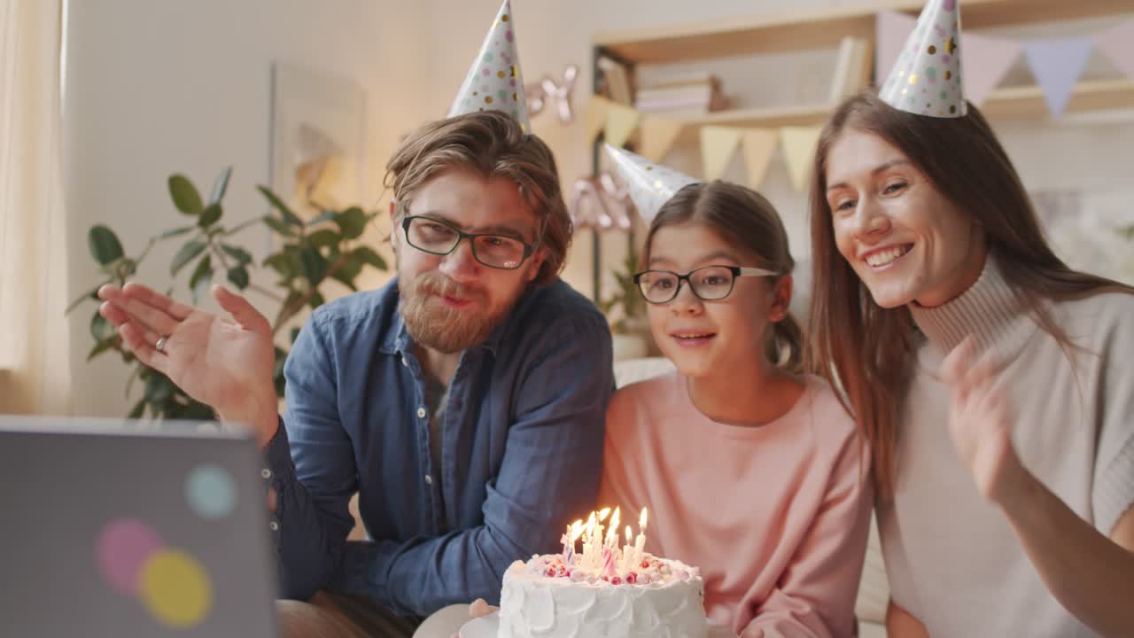padres e hija celebrando el cumpleaños con sombreros de cumpleaños, saludando a la cámara con un pastel de cumpleaños