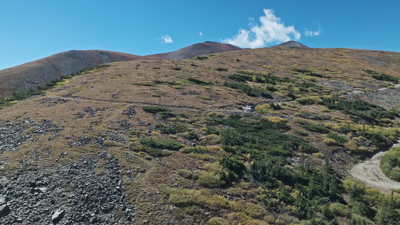 Aerial orbit around evergreen trees and rocky grassy hills of the alpine landscape as car drives on Peak 10 trail Breckenridge Colorado