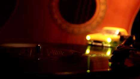 slider shot. disco de vinilo vintage tocando en el reproductor y la guitarra acústica en el fondo con humo de naranja de fuego. concepto de crimen o blues con instalación de automóvil de juguete. enfoque selectivo