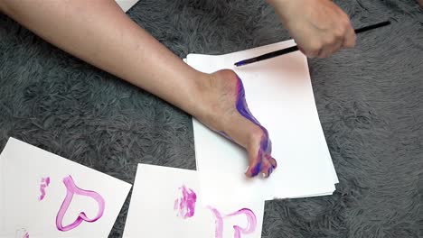 person delicately strokes paintbrush across bottom of foot on carpeted ground