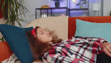 tired preteen girl child kid lying down in bed taking a rest at home, napping falling asleep on sofa