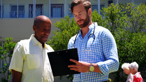 Front-view-of-active-African-American-senior-man-and-male-doctor-discussing-over-medical-report-in-t