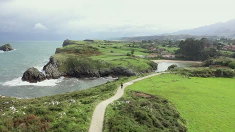 Aerial-view-of-a-man-walking-on-a-road,-at-Playa-Poo-beach,-in-North-Spain---circling,-drone-shot