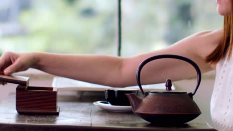 mano de mujer vista vertiendo agua caliente infundida con té de hierbas orgánicas de una tetera asiática vintage - cámara lenta aislada