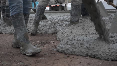 concrete is poured as workers with shovels pave a street