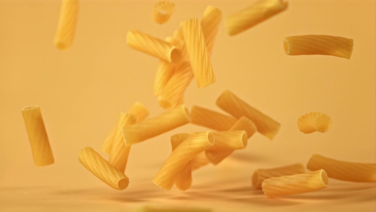 Maccheroni secchi che cadono al rallentatore su sfondo giallo