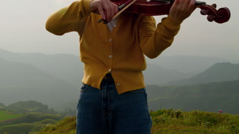 camera moves up to show a woman playing a violin with her eyes closed on a magical misty mountain