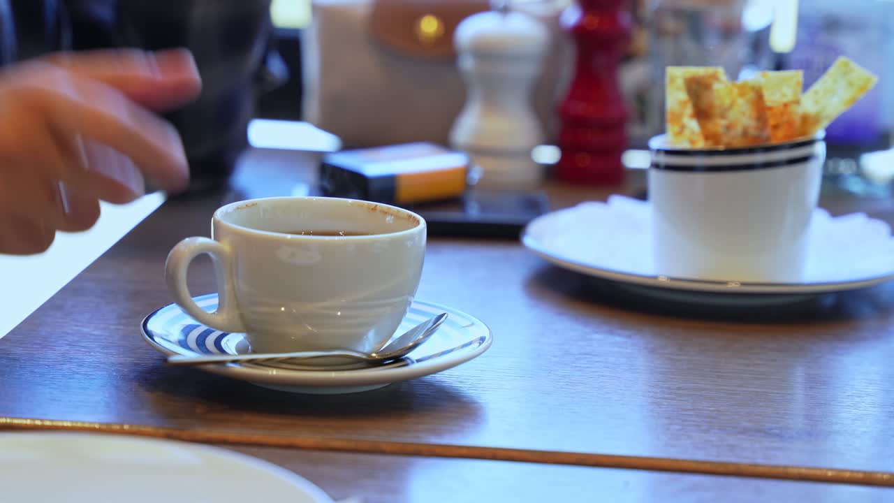 Smooth motion of a hand lifting and placing a steaming coffee cup on a café table, ideal for lifestyle, beverage ads, or relaxation content