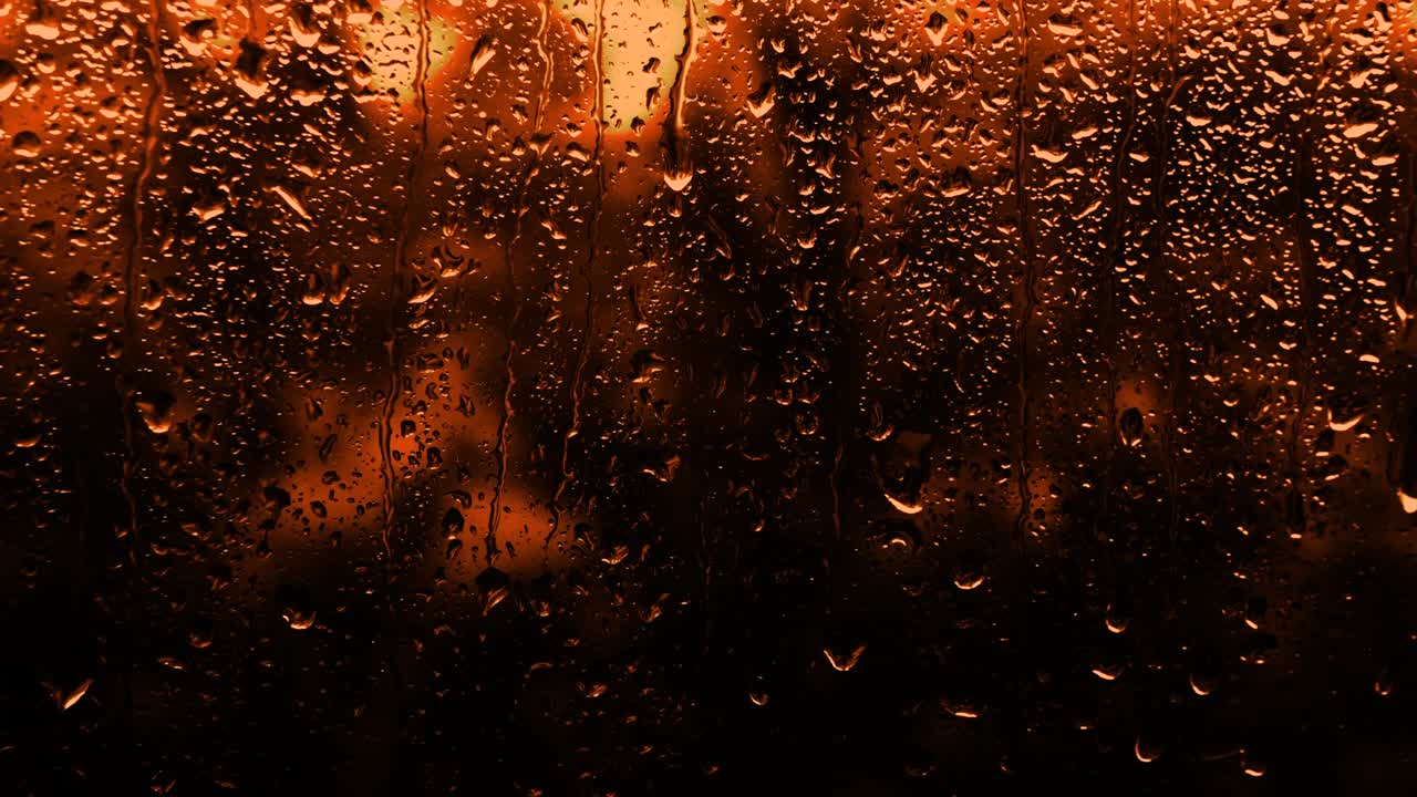 Rainy background in neon orange color, drops flow down the glass with warm tones of flowers, copy the space background. The texture of raindrops on the glass