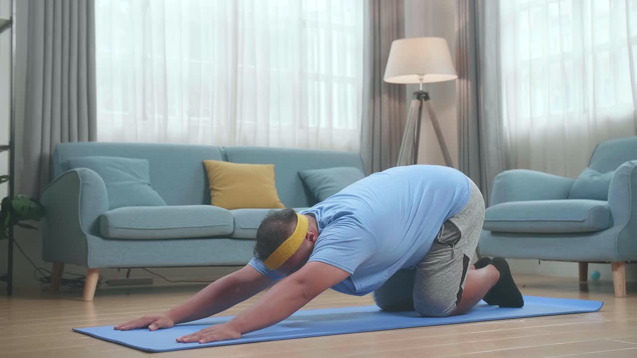 한 아시아인 남자가 집에서 마트에 몸을 구부려 위쪽으로 향하는 요가를 하고 있습니다.