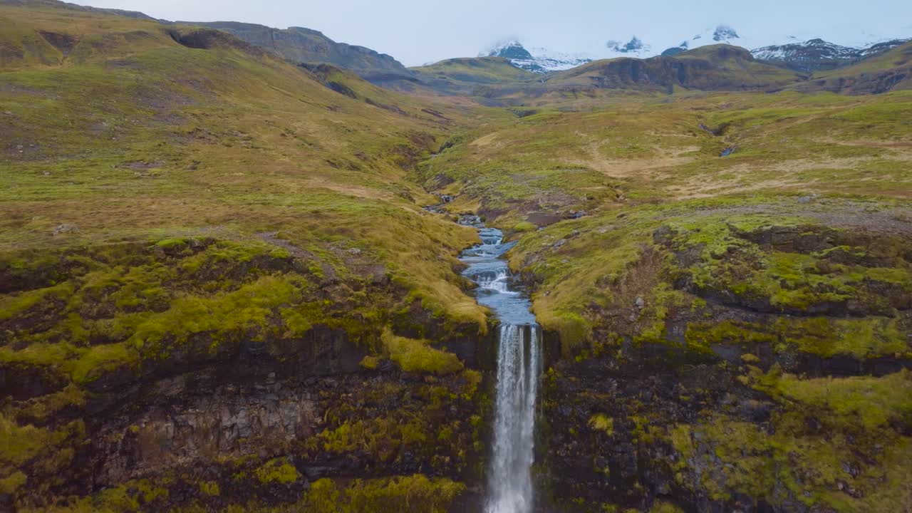 imagen aérea de un dron de una cascada en islandia con picos nevados en el fondo
