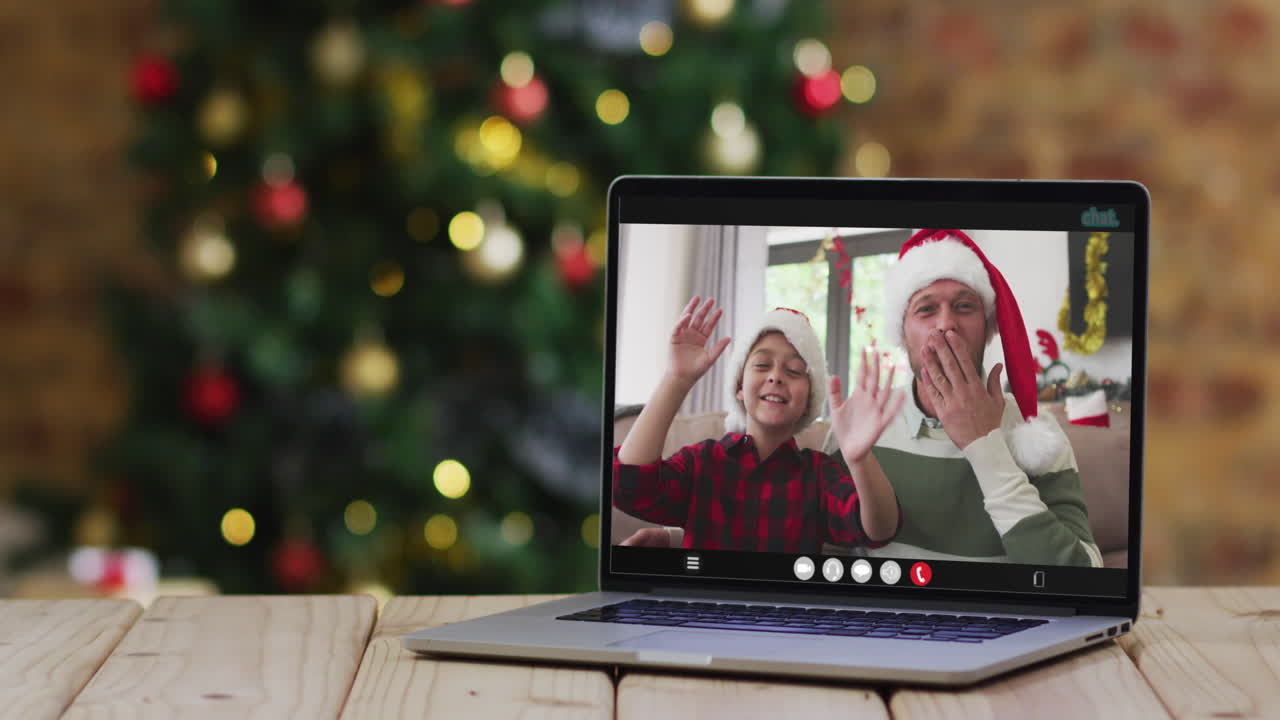 padre y hijo felices saludando en una videollamada en una computadora portátil, con decoraciones de navidad y árbol