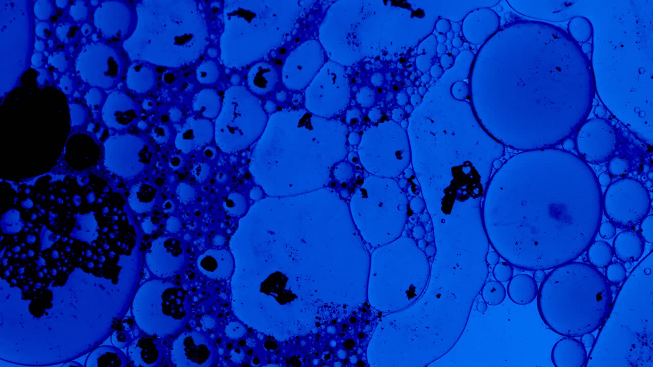 sfondo astratto blu con gocce d'olio e macchie di inchiostro nero che galleggiano su un liquido come batteri