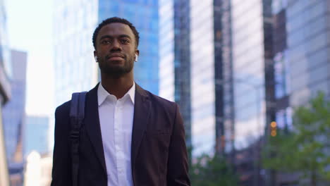 young businessman wearing wireless earbuds streaming music or podcast from mobile phone walking to work in offices in the financial district of the city of london uk shot in real time 1