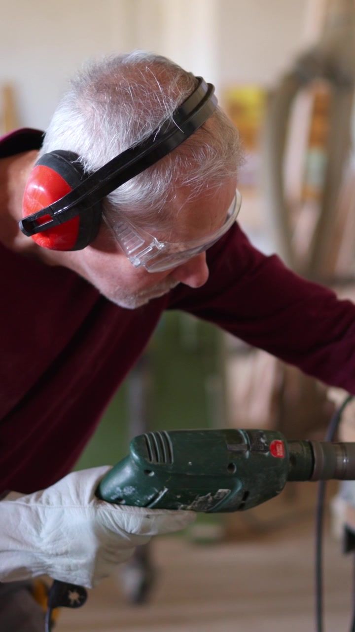 Close-up van een oudere man die boort met veiligheidsuitrusting in een werkplaats