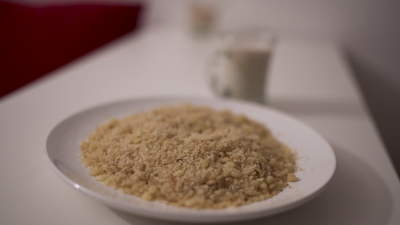 Close-up of traditional reviro dish placed in a white bowl, with textured grains in focus and a milk glass blurred in the background — captured in a slow motion orbit shot with soft depth