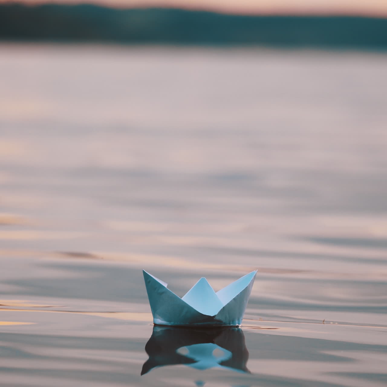 Blue homemade boat on water on blurred evening background. Paper little ship floating alone in calm river at sunset.
