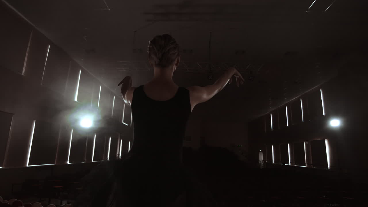 A ballerina dances in a hall with empty seats. A female dancer enjoys the quiet of an empty scene and no audience