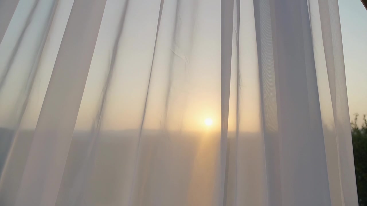 Billowing sheer curtain panels shifting and diffusing sunlight at window as sun rising