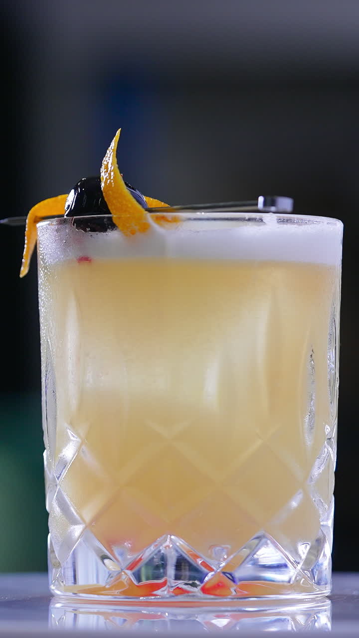 Beautifully decorated cocktail in the wide glass on the rotating white table. Beverage served in the bar. Close up. Blurred backdrop. Vertical video