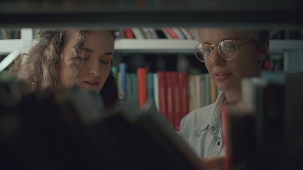Two Female Friends Discussing Books on Shelf in Public Library