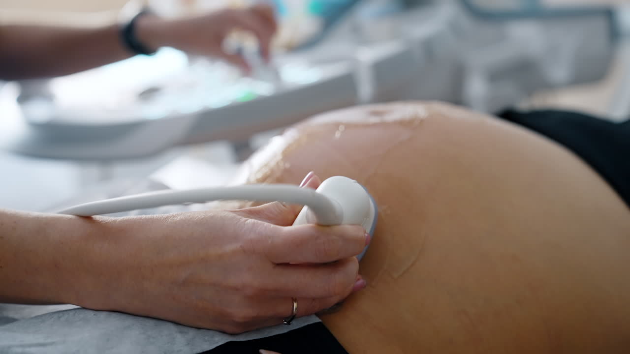 Doctor's hand moving the device by the big gelled belly of pregnant. Ultrasonic examination of pregnancy development.