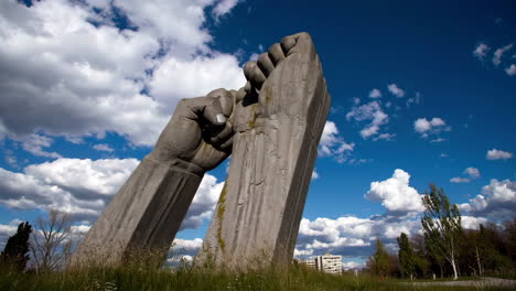 close-up of a weathered stone sculpture of a hand holding a column against a cloudy sky