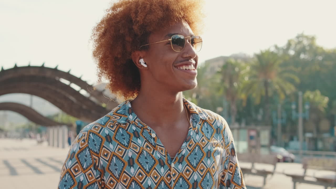 Giovane uomo sorridente con capelli ricci e occhiali da sole all'aperto