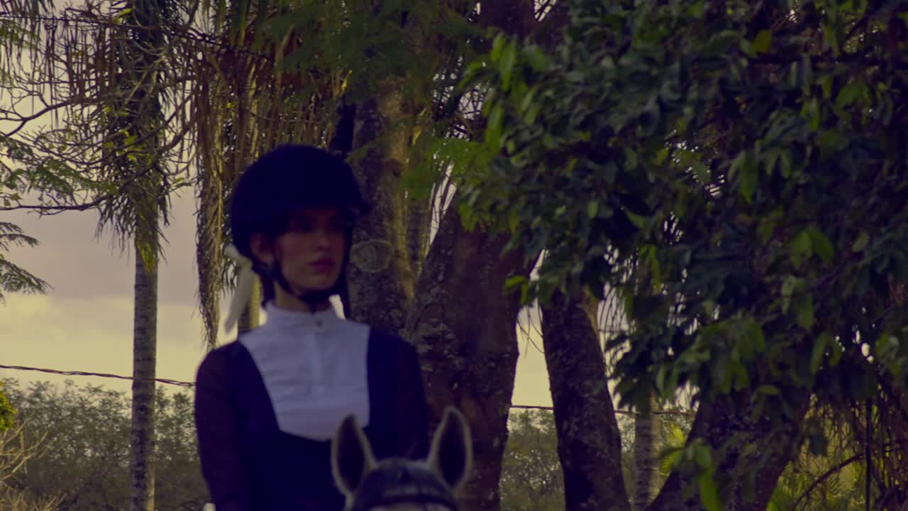 Cinematic slow motion shot of a beautiful woman riding a white horse towards the camera while wearing a black and white outfit with matching white horse riding gloves