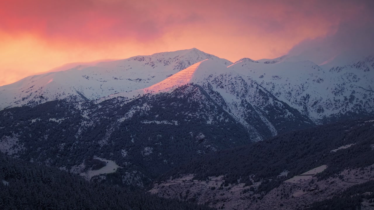 Slow drone panning over snowy mountain range at sunset with pink sky in Andorra
