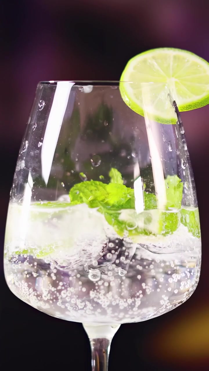 Un cocktail mojito con lime e menta in un bicchiere, su uno sfondo sfocato e colorato