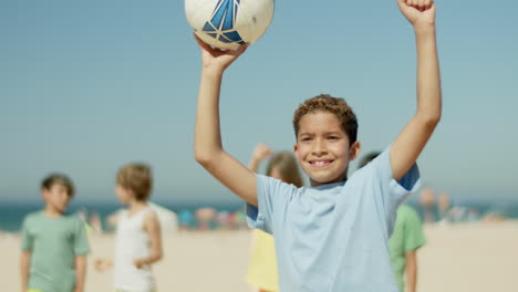 medium shot of happy boy raising hand with soccer ball in it up