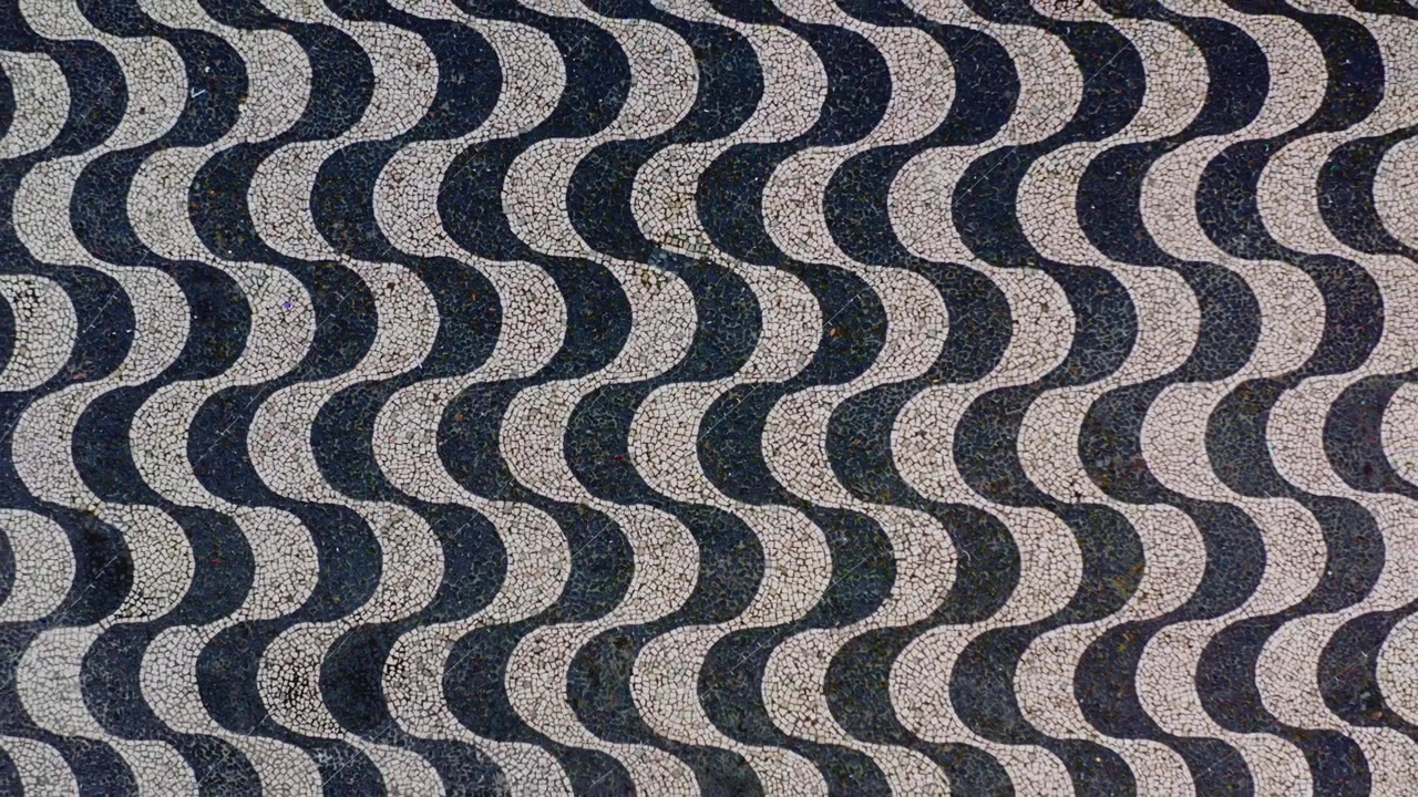 Top down aerial drone flight over the black and white wave cobblestone mosaic of Largo de Sao Sebastiao plaza, Portuguese pavement pattern filling the frame, abstract graphic texture, Manaus, Brazil.