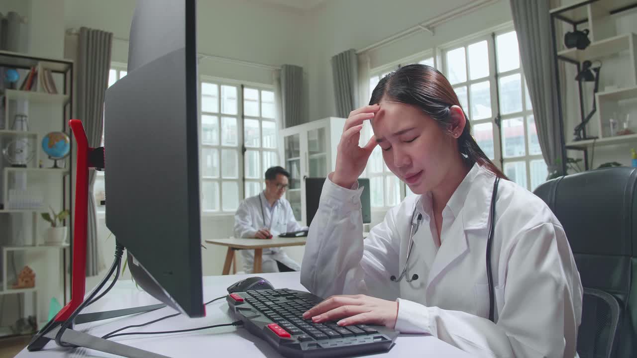 Young Asian Woman Doctor Is Using Computer And Headache In Workplace. Medical Concept