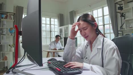 young asian woman doctor is using computer and headache in workplace. medical concept