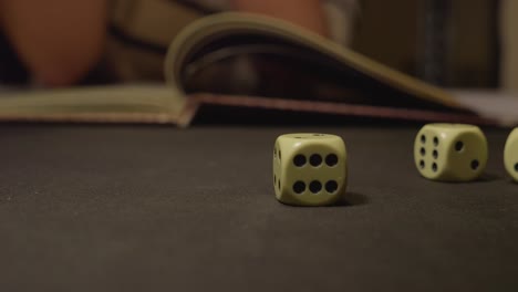 throwing ivory six face dices on black table with role book in background