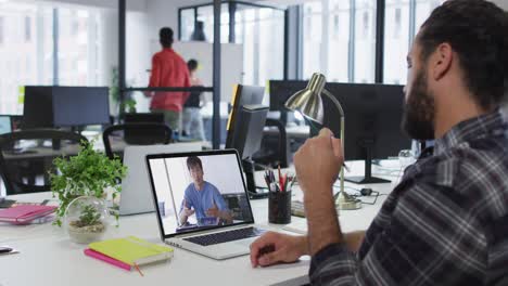hombre de negocios de raza mixta sentado en un escritorio usando una computadora portátil haciendo una videollamada con un colega masculino