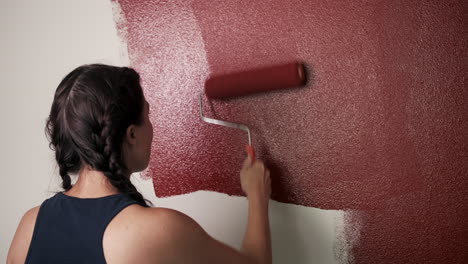 young woman paints red wall in house