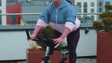 Athletic-woman-riding-on-spinning-stationary-bike-training-routine-on-house-rooftop,-weight-loss